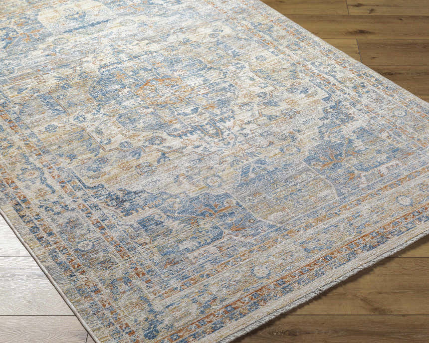 Close-up of the Bora Area Rug on wood floor. Traditional rug design in camel, copper, dark gray, and lambswool. Corner