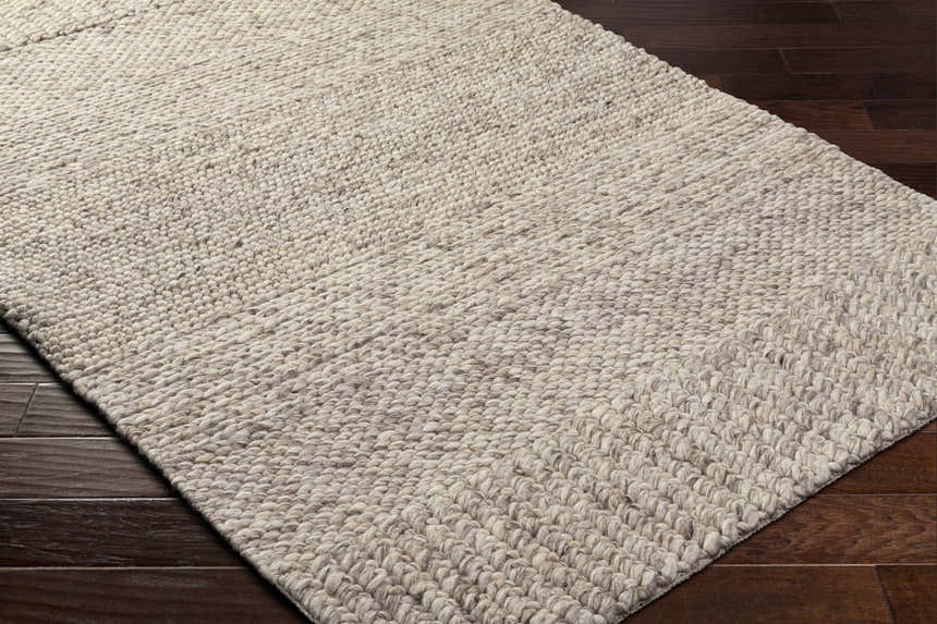 Close up of the hand woven Nimai Beige Wool Area Rug showing texture and detail on dark wood floor. Corner
