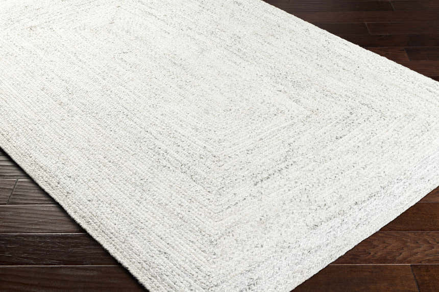 Close-up of the hand-woven Kenyi Rose Cream Area Rug showing its beige, gray, and white texture on dark wood floors. Corner