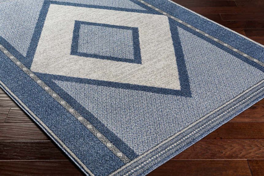 Close-up of the Onan Area Rug, a machine-woven rug with diamond pattern in arctic sky, gray, light gray, and silver. Corner