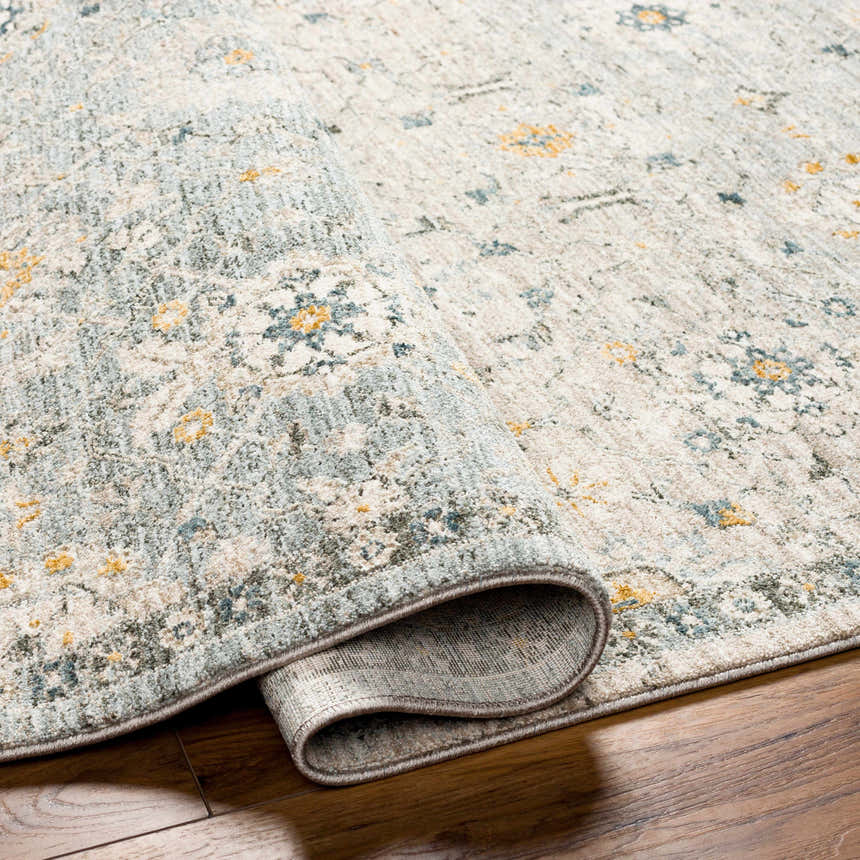Close-up of the Annie Green Textured Rug, a machine-woven cotton rug with a traditional floral pattern in green, blue, and yellow. Fold