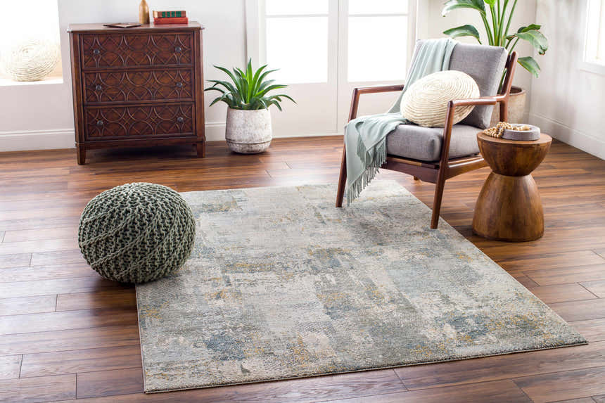 Living room scene with a gray chair, wood accents, and the Elina Textured Abstract Rug in dusty sage, blue, and gray. Roomscene-Rectangle