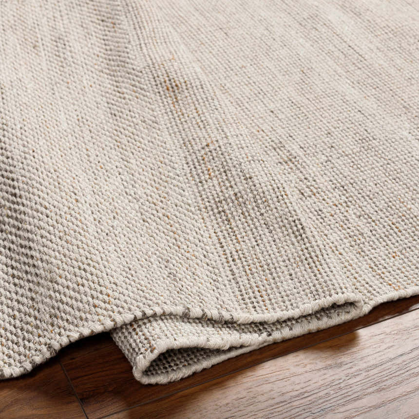 Close-up of the Anaya Beige Area Rug showing its hand-woven texture and neutral colors on a wood floor. Fold