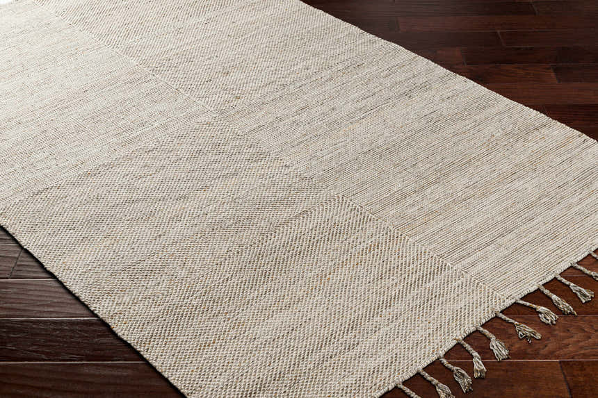 Close up of the Anaya Beige Area Rug showing its hand woven texture and tassel detail on dark wood floor. Corner