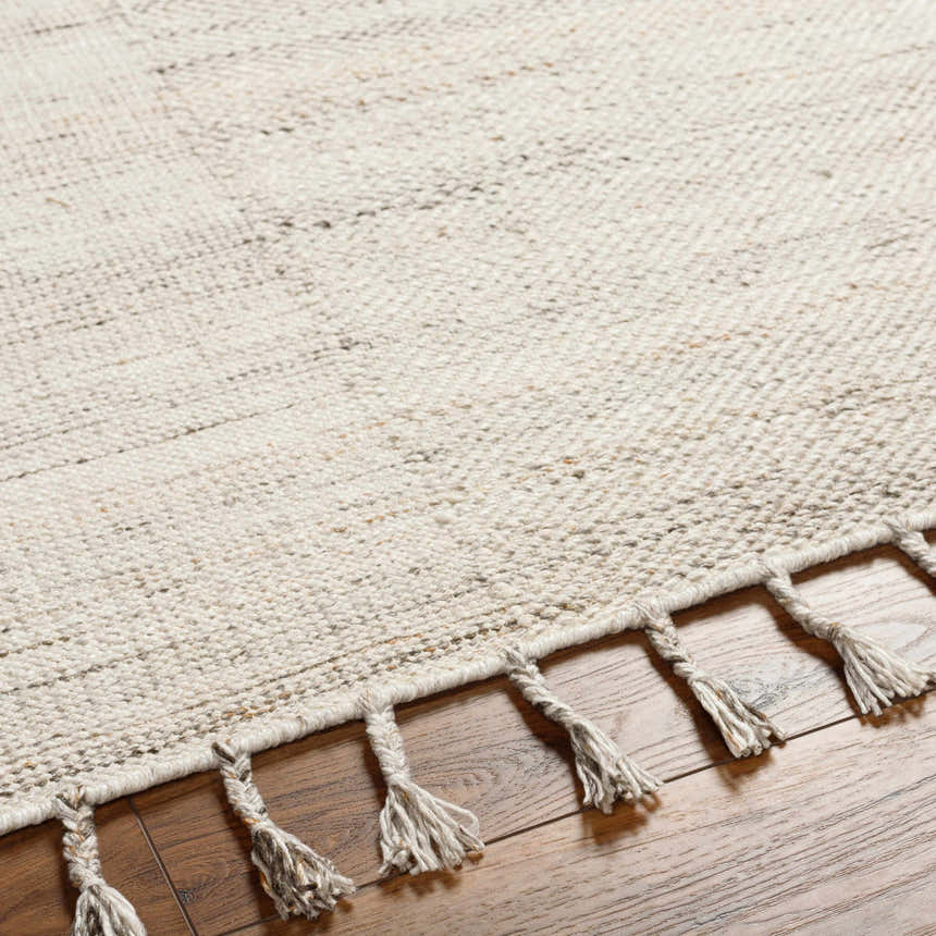 Close-up of the hand-woven Anaya Cream Area Rug showing beige tones, subtle pattern, and decorative tassels on wood floor. Texture