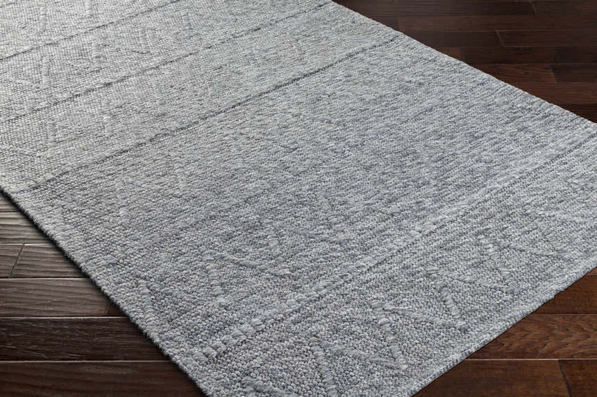 Close-up of the Kyung Dark Gray Area Rug showing its woven texture and subtle geometric pattern on dark wood flooring. Corner