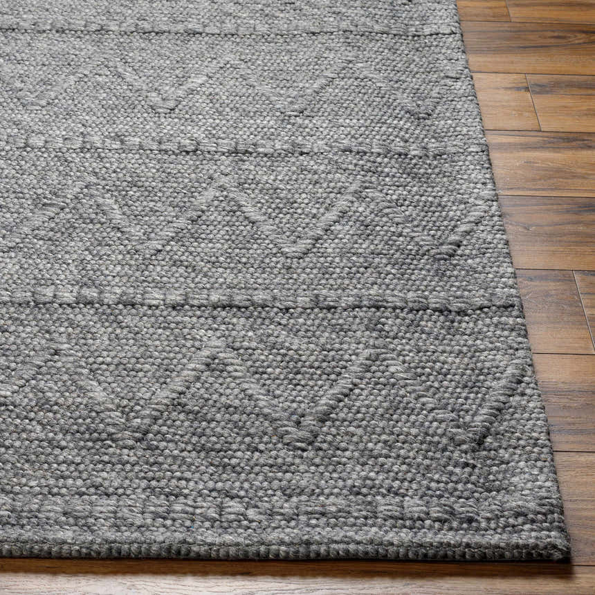 Close-up of the hand woven Kyung Dark Gray Area Rug showing its texture and geometric pattern on a wood floor. Front