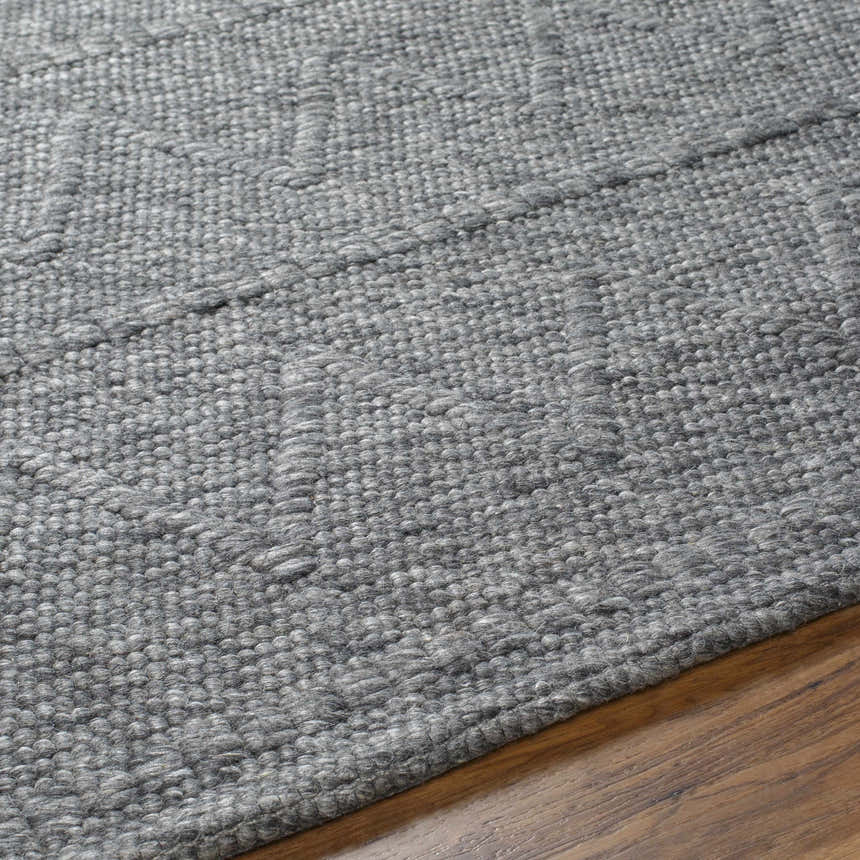 Close-up of the hand-woven Kyung Dark Gray Area Rug showing its texture and subtle geometric pattern on a wood floor. Texture