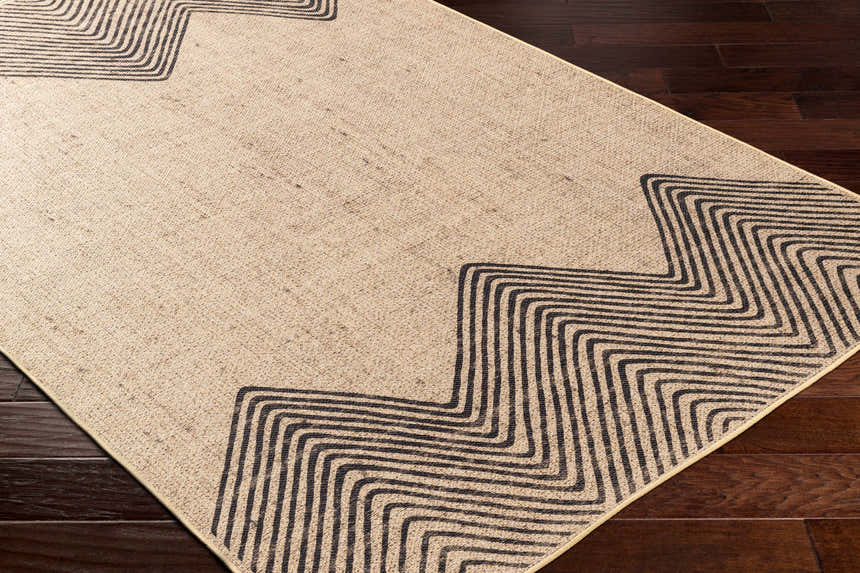 Close-up of Suzy Washable Jutely Rug in camel with a charcoal geometric pattern on dark wood floors. Corner