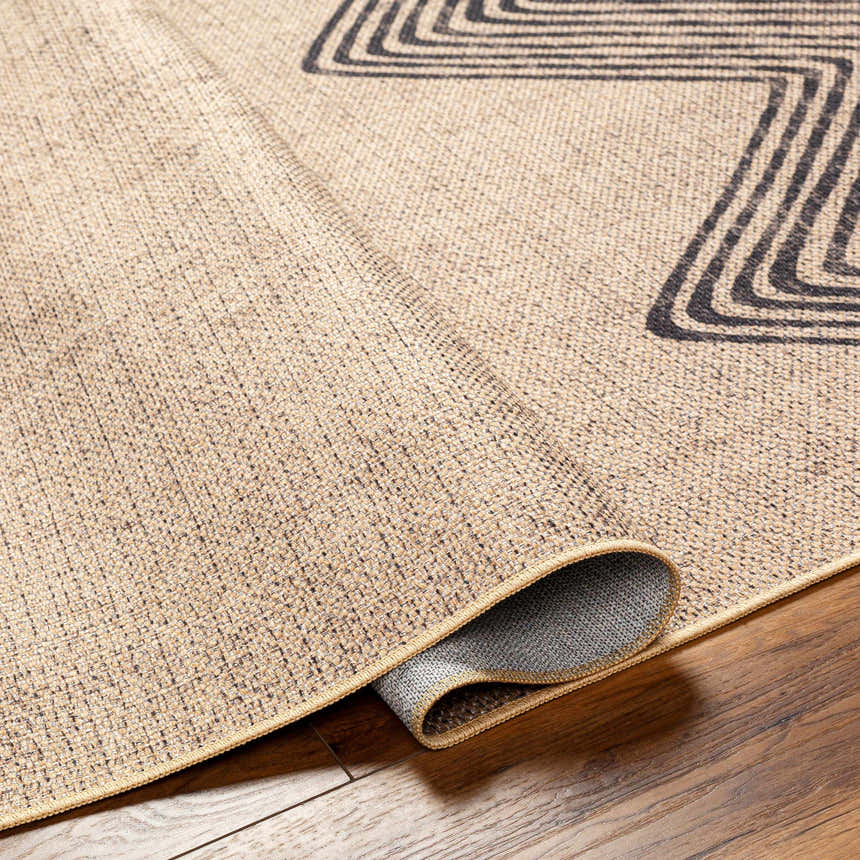 Close-up of the Suzy Washable Jutely Rug in camel with a charcoal geometric pattern and jute texture on a wood floor. Fold