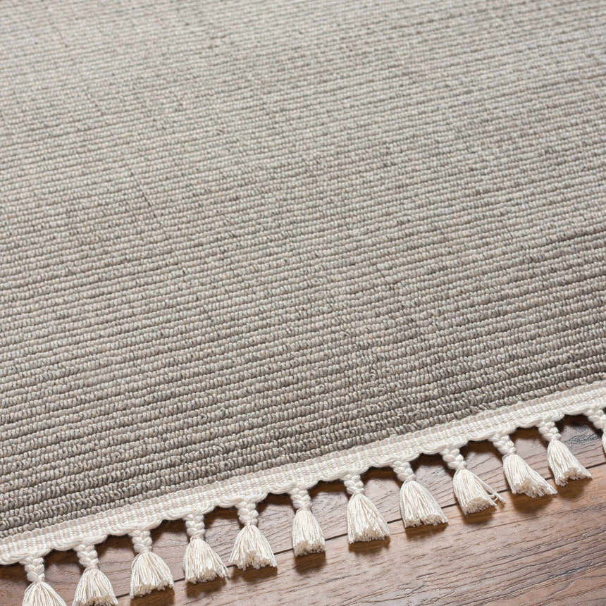 Close-up of the Abia Gray Area Rug showing its woven texture and cream tassels on a wood floor. Texture