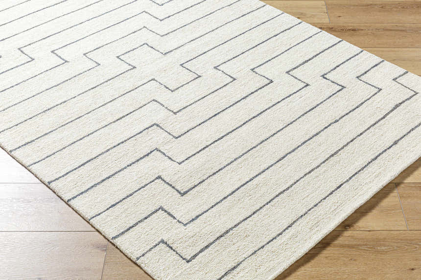 Close-up of a hand-tufted Wyome Area Rug. Off-white wool rug with a geometric, zig-zag pattern. Farmhouse style. Corner