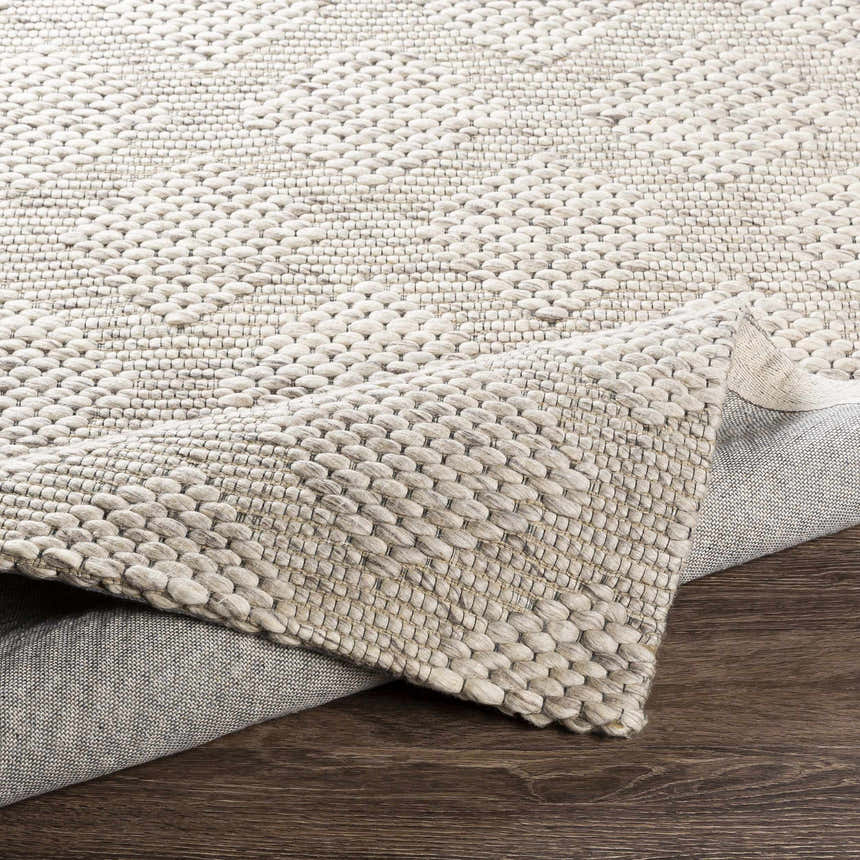 Close up of the hand woven Sauget Area Rug, showing its off white, gray, and black contemporary design and wool texture. Fold