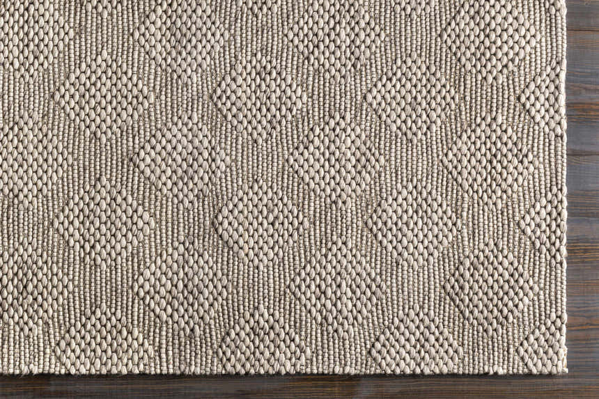 Close up of the hand woven Sauget Area Rug with a textured, contemporary design. Black, gray, and off white. Corner