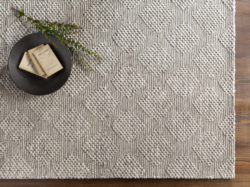 Close-up of the Sauget Area Rug. Hand-woven rug with a textured, geometric pattern in black, gray, and off-white. Styleshot