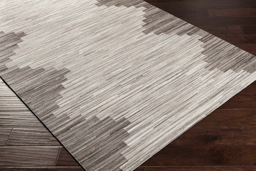 Close-up of Shearwater Premium Rug showing beige, charcoal, and cream stripes with a geometric border on dark wood floor. Corner