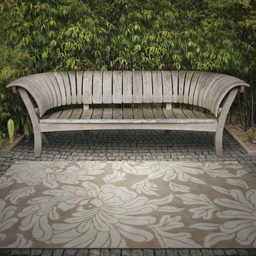 Outdoor scene with a beige Sherard Area Rug featuring a floral pattern under a wooden bench. Roomscene-Rectangle