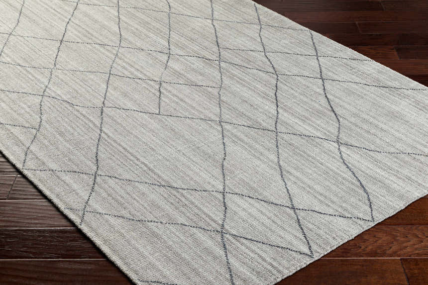 Close-up of the Nari Light Gray Area Rug. Farmhouse style rug with charcoal geometric pattern on a textured light gray background. Corner