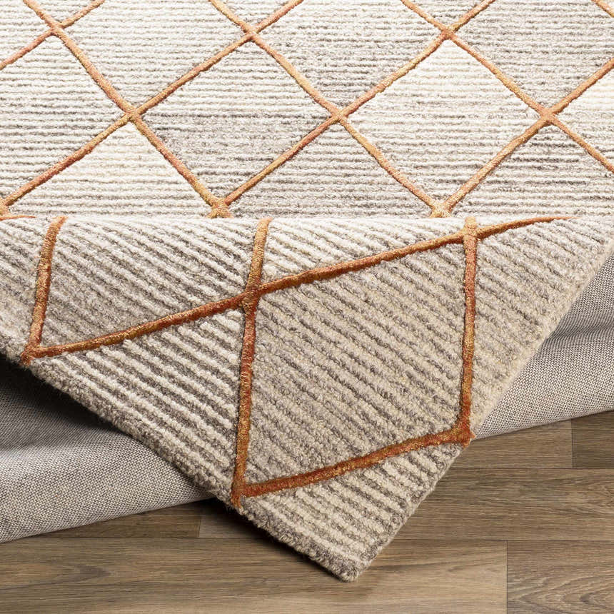 Close-up of the Sharpes Area Rug. Hand-tufted wool rug with geometric diamond pattern in brown, mustard, and orange tones. Fold