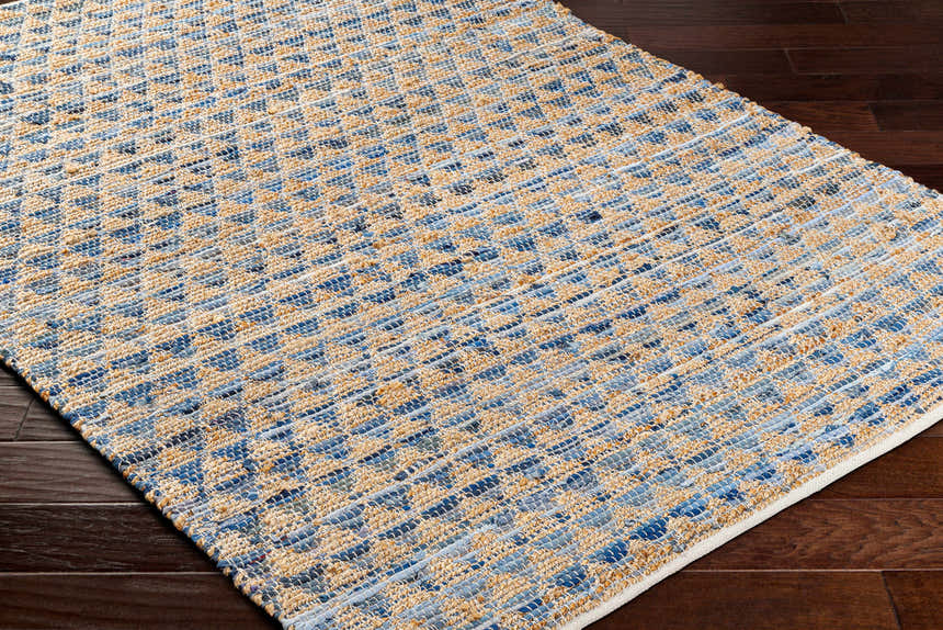 Close-up of the Colm Recycled Blue Jean Rug. Hand-woven rug with a geometric pattern in shades of blue and tan. Corner