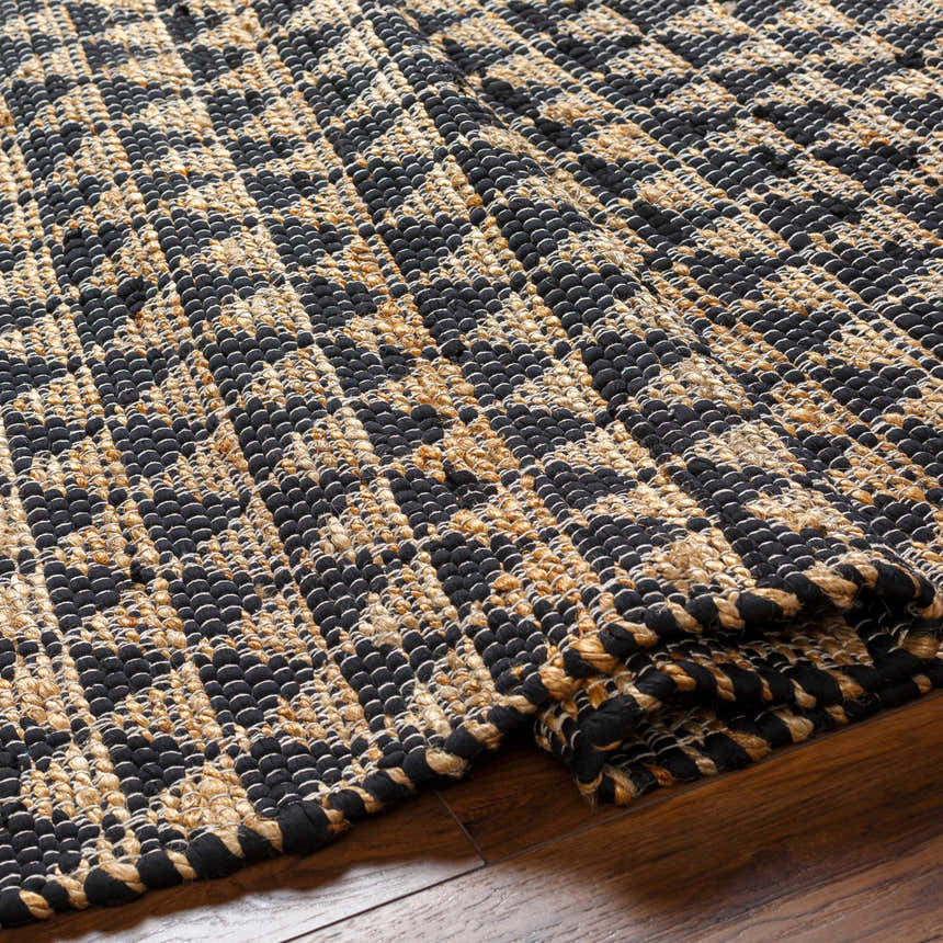 Close-up of the Colm Recycled Black Jean Rug showing its hand-woven texture and geometric black and jute pattern. Fold