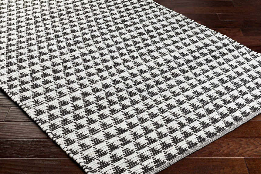Close-up of the Gzifa Jute Rug showing a black and white houndstooth pattern and hand woven texture. Corner