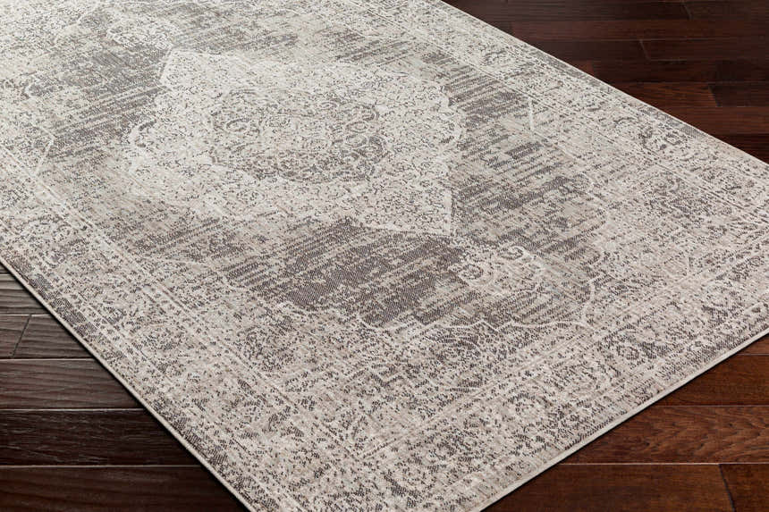 Close up of the Azibo Area Rug showing its traditional, farmhouse design and neutral colors on dark wood flooring. Corner