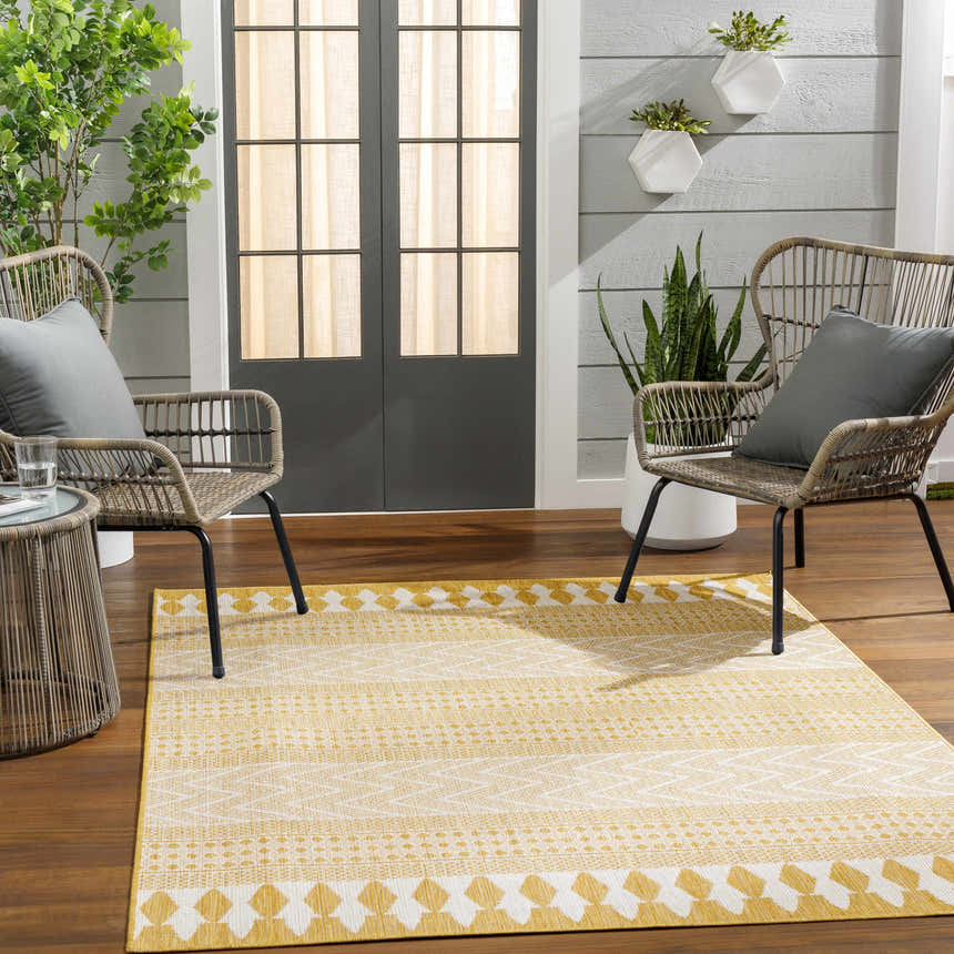 Outdoor patio scene with the Asif Mustard Area Rug, wicker chairs, wood floors, and potted plants. Roomscene-Rectangle