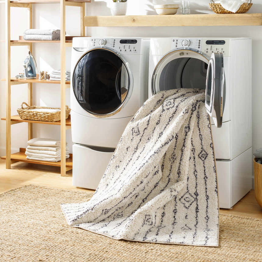 Laundry room scene with a Demi Beige Washable Area Rug coming out of the dryer, jute rug underneath. Washing-Machine
