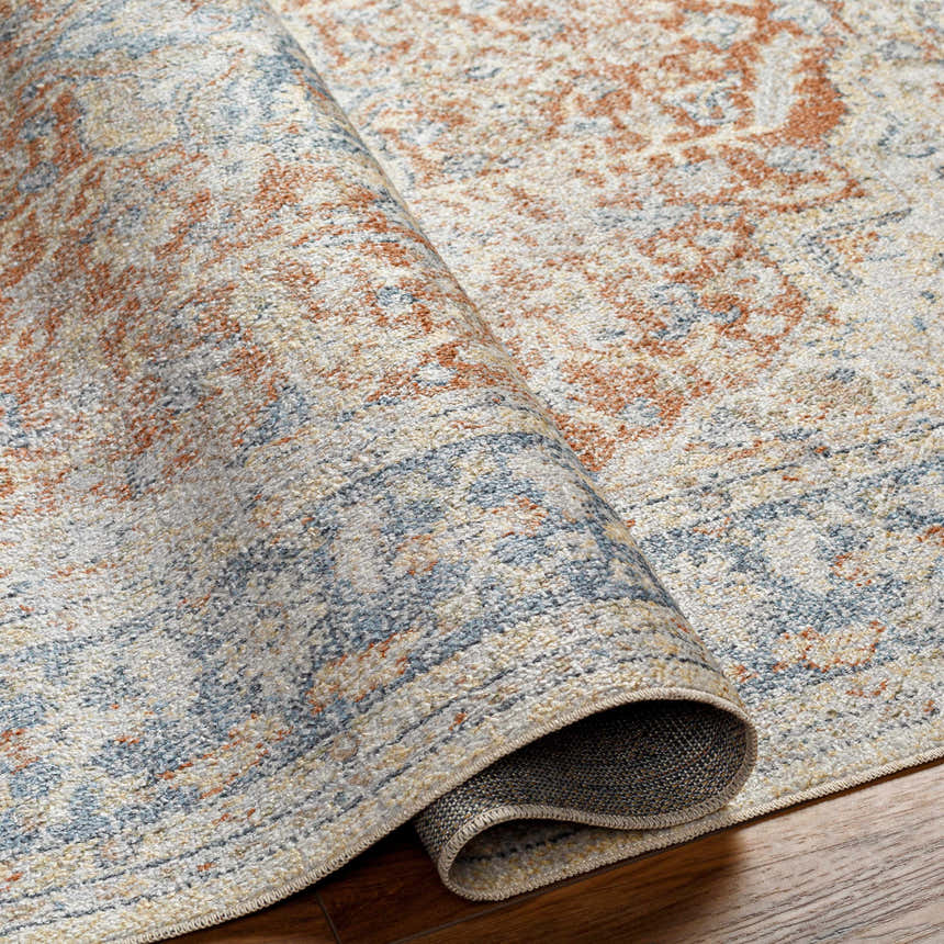 Close-up of the Emke Rust Washable Area Rug showing its faded driftwood, nutmeg, and dark gray traditional pattern. Fold