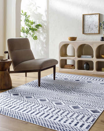 Living room scene with a gray chair and Sanyu Washable Area Rug in gray and off-white with a geometric pattern. Roomscene-Rectangle