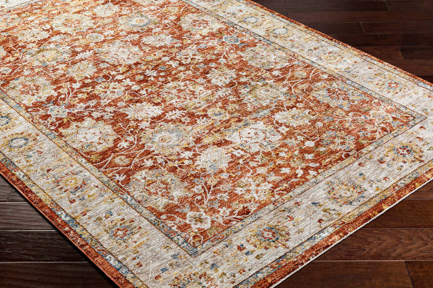 Close-up of the Duong Rust Textured Rug showing its brick red, sage, and blue floral pattern and textured weave. Corner