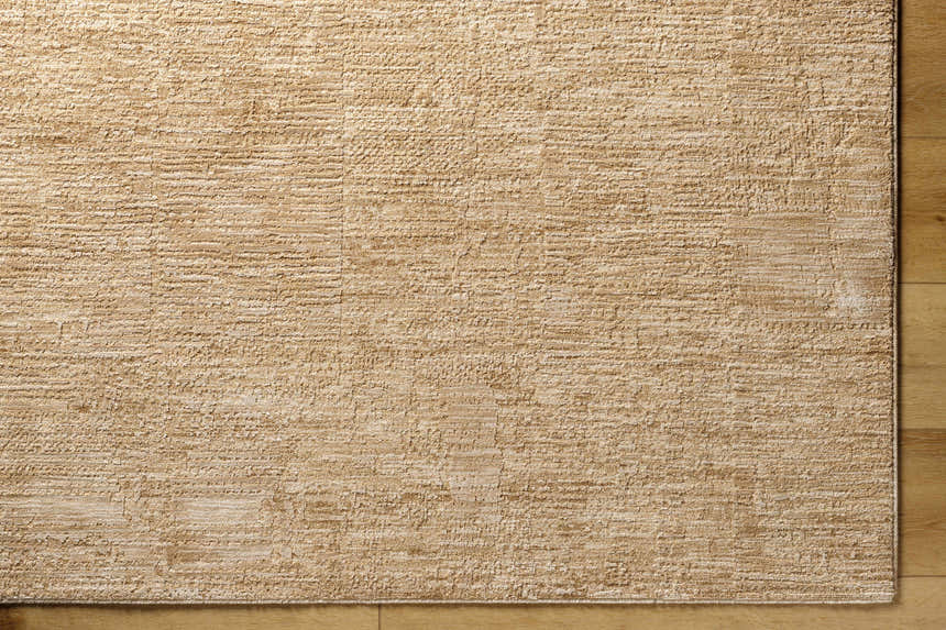 Close-up of the tan Kahua Area Rug showing its subtle texture and machine-woven construction on a wood floor. Corner
