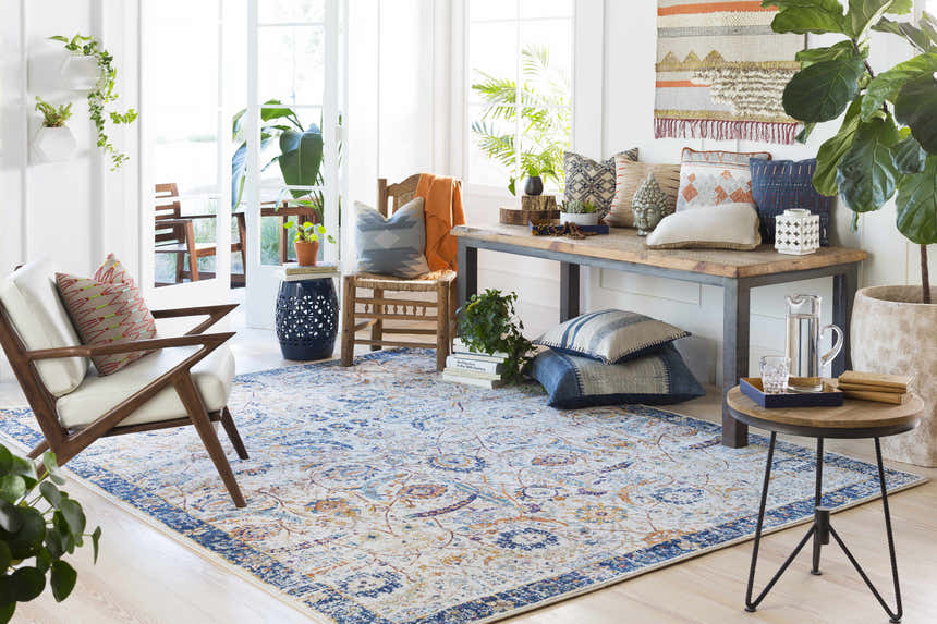 Bright living room with a Smyrna Area Rug in blue, orange, and beige floral pattern. Bohemian style with plants and eclectic decor. Roomscene-Rectangle