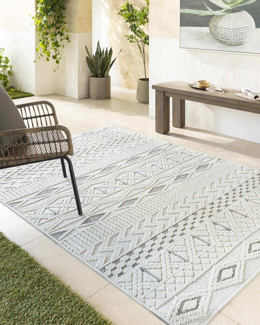 Sunlit patio with a cream Sokka Area Rug, woven chair, wooden bench, and potted plants. Roomscene-Rectangle