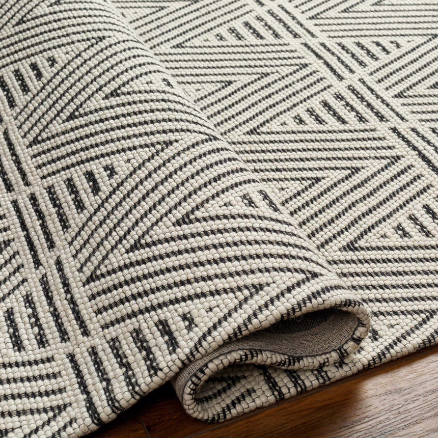 Close-up of the Dawid Wool Area Rug, showcasing its black and bone geometric pattern and hand-woven texture. Fold