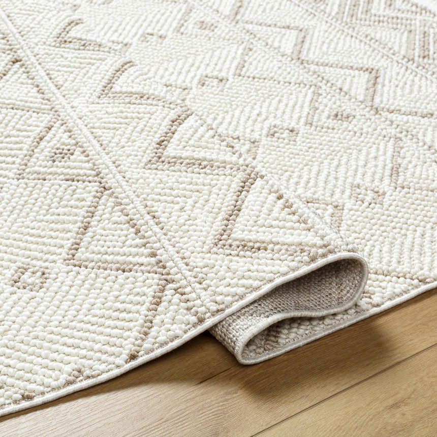Close-up of the Armen Area Rug showing its beige and cream geometric pattern and textured, machine-woven construction. Fold