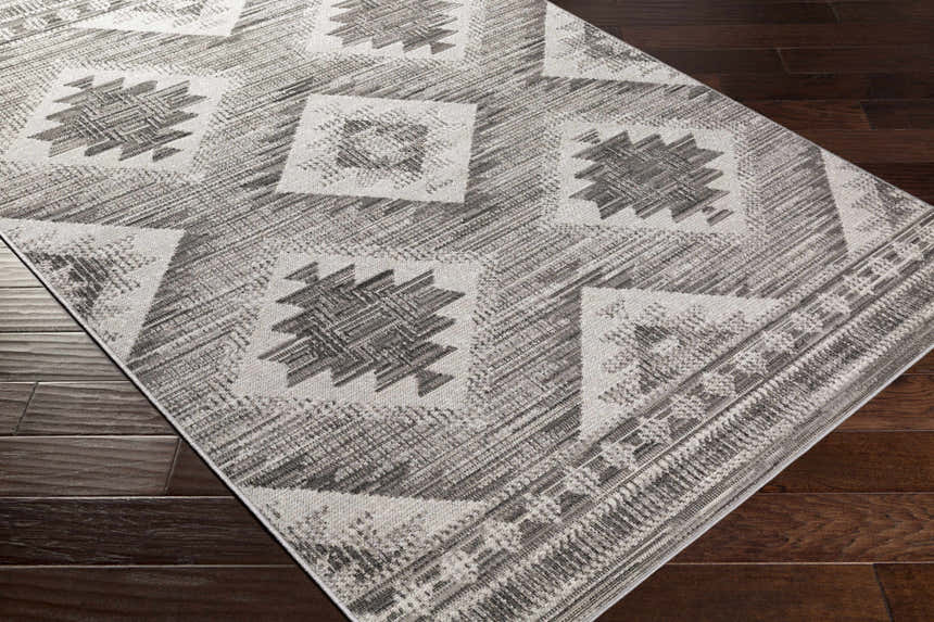 Close-up of the Spade Area Rug. Black, light gray, and white geometric pattern on a machine woven, rectangular rug. Corner
