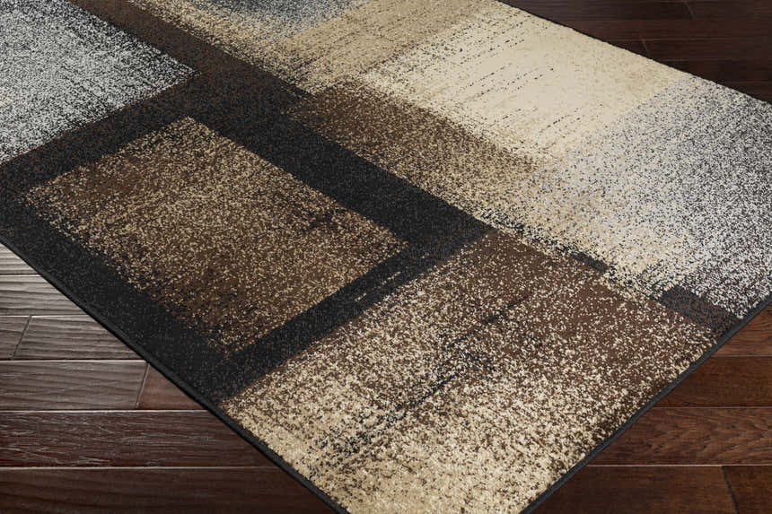Close-up of the Spraggs Area Rug showing a geometric pattern in black, charcoal, brown, beige, and gray. Corner