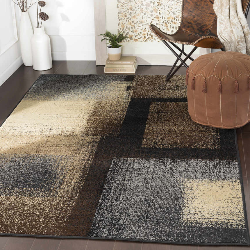 Living room scene with a Spraggs Area Rug in black, brown, gray, and beige, styled with a leather chair and brown pouf. Roomscene-Rectangle