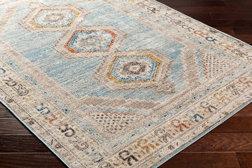 Close-up of the Iresh Area Rug. Farmhouse style rug in cloud gray, beige, brown, and blue geometric pattern. Corner