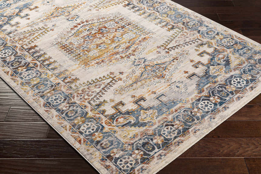Close-up of the Espy Area Rug showing its brick red, burnt orange, and blue traditional pattern on dark wood floors. Corner