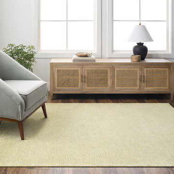 Living room scene with Isako Solid Lime Washable Area Rug, gray chair, wood cabinet, and natural light from windows. Roomscene-Rectangle