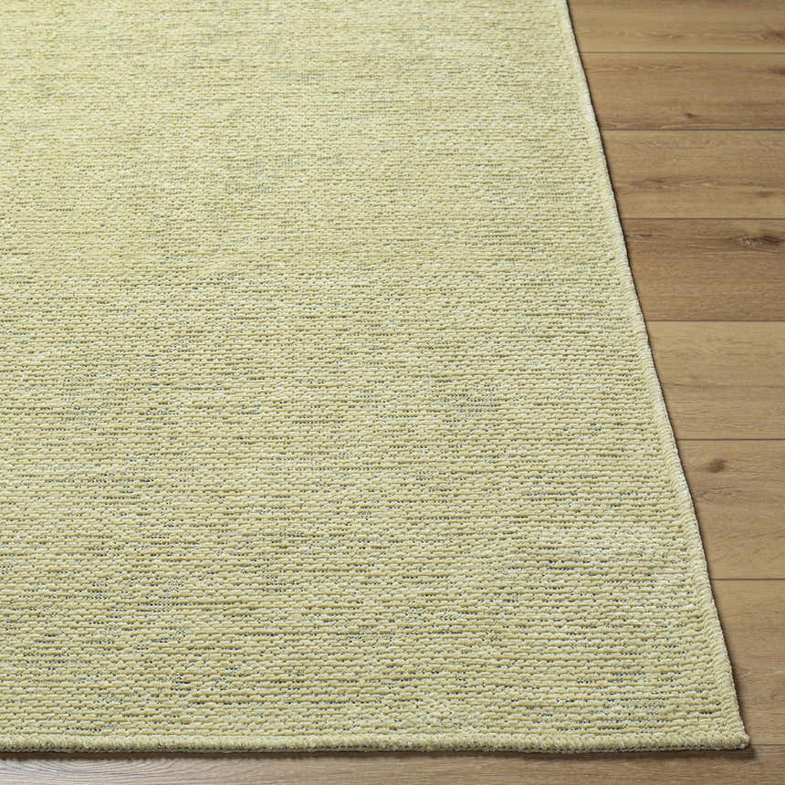 Close-up of the Isako Solid Lime Washable Area Rug showing its woven texture and soft lime green color on wood floor. Front