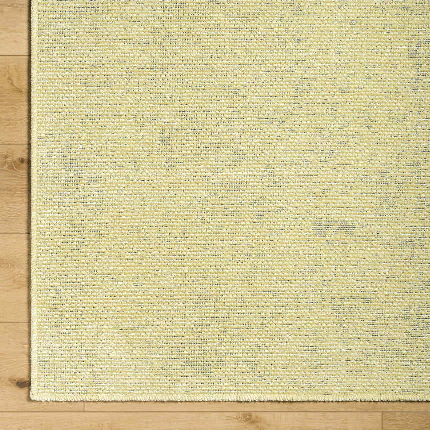 Close-up of Isako Solid Lime Washable Area Rug showing texture and color variations on light wood floor. Corner