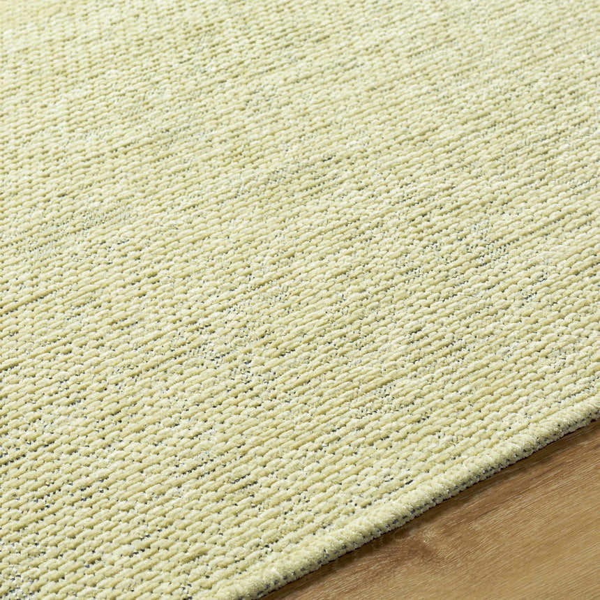 Close-up of the Isako Solid Lime Washable Area Rug showing its plush texture and subtle lime green color on a wood floor. Texture