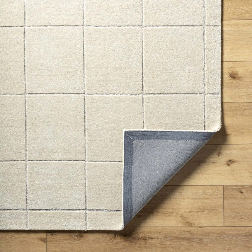 Close-up of the Siarl Cream Checkered Area Rug showing the wool texture, beige color, and gray backing on wood floor. Fold