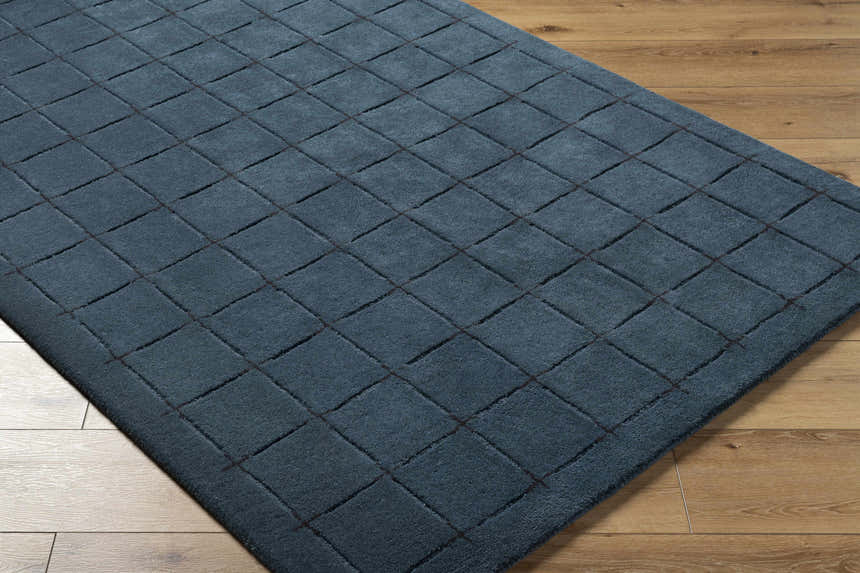 Close-up of the hand-tufted Sanvi Navy Wool Area Rug featuring a geometric square pattern on a light wood floor. Corner