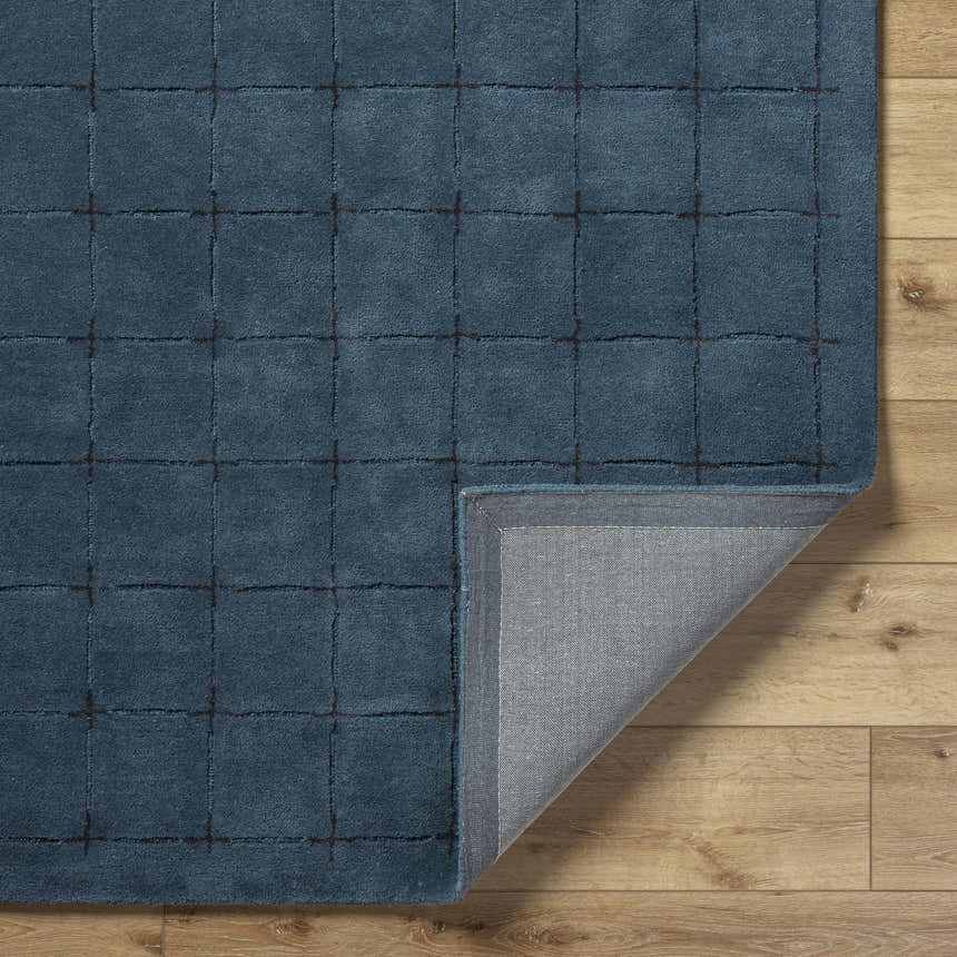 Close-up of the hand-tufted Sanvi Navy Wool Area Rug, showing its navy blue color and grid pattern on a wood floor. Fold