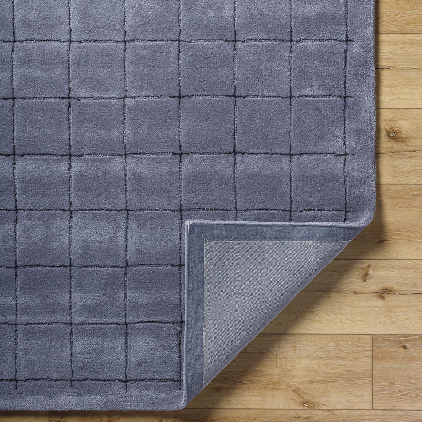 Close-up of the hand-tufted Sanvi Charcoal Area Rug showing its wool texture and contemporary square pattern on wood floor. Fold